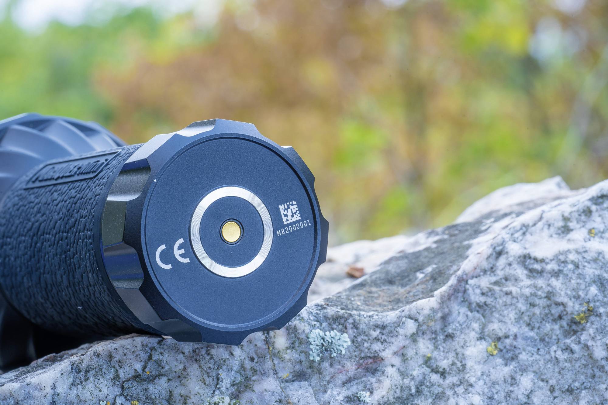 Fernglas auf einem Felsen liegend mit Fokus auf die Unterseite. Umgebung unscharf und herbstlicher Hintergrund mit Bäumen.