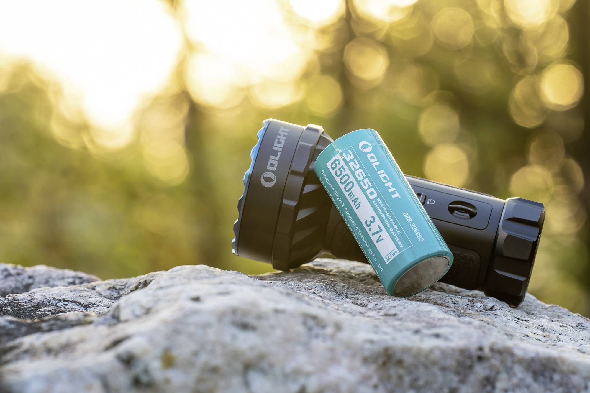 Eine Taschenlampe und ein Akku liegen auf einem Felsen in natürlicher Umgebung. Sonnenstrahlen leuchten im Hintergrund.