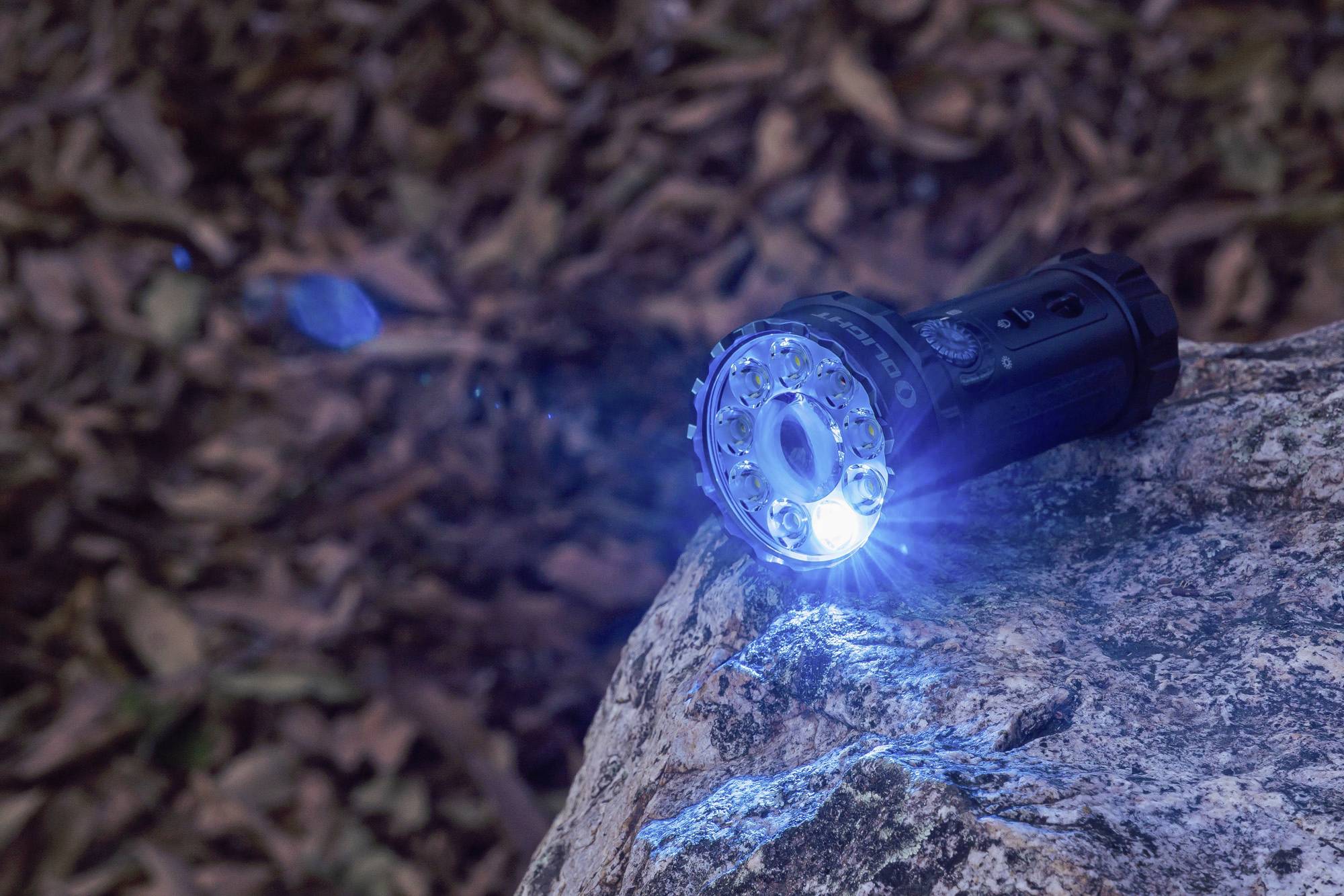 Taschenlampe liegt auf einem Felsen und leuchtet blau. Im Hintergrund sind unscharfe Blätter zu sehen.