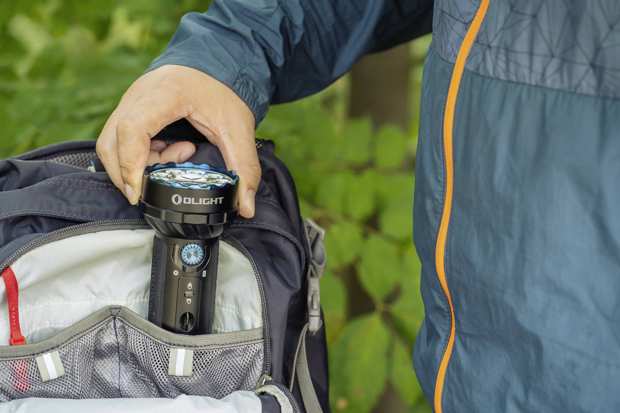 Eine Person steckt eine Taschenlampe in einen Rucksack. Sie trägt eine blaue Jacke.