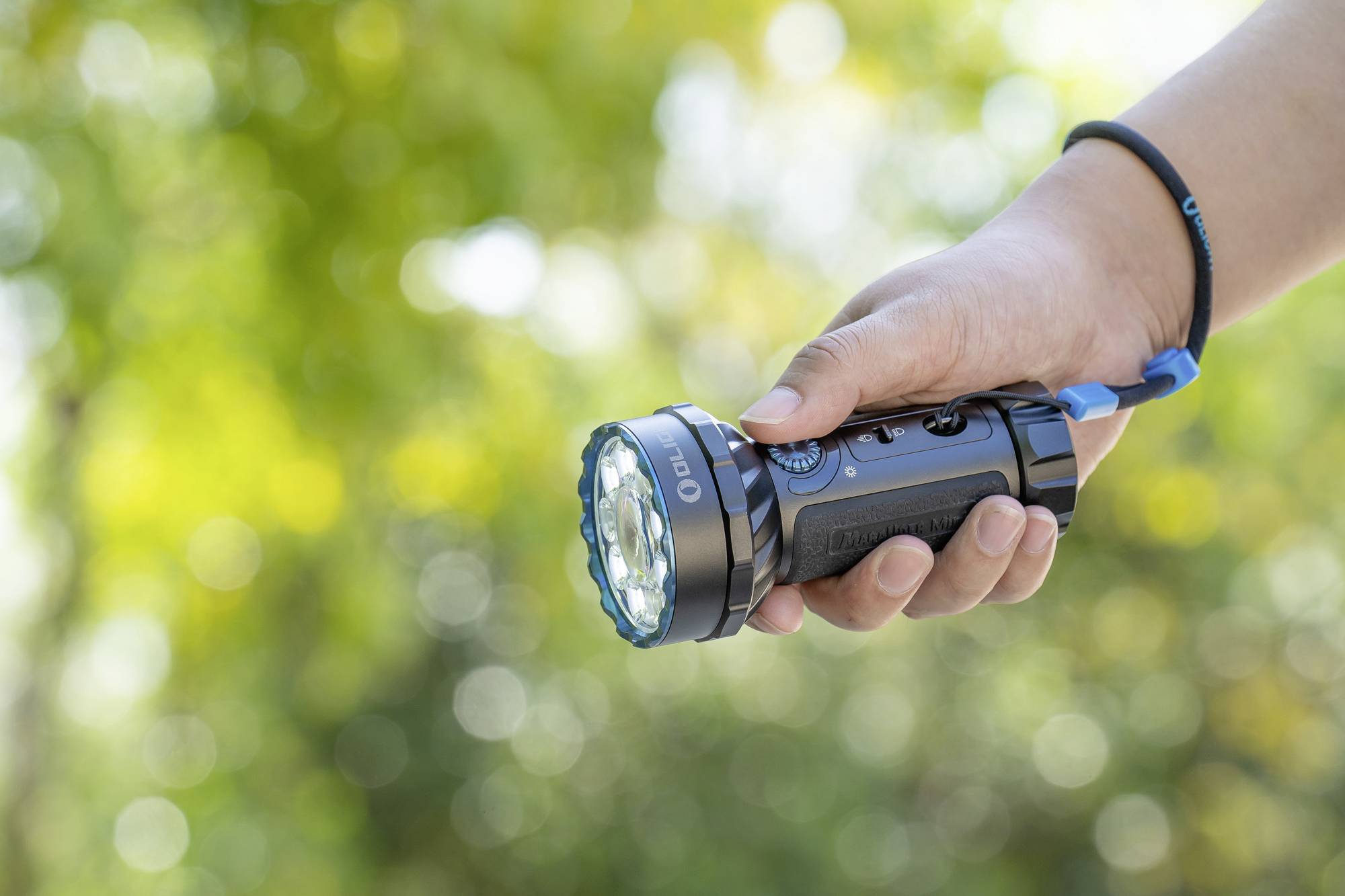 Eine Hand hält eine eingeschaltete Taschenlampe, umgeben von unscharfem grünem Hintergrund im Freien.
