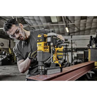 Eine Person bohrt mit einer gelben, bürstenlosen Bohrmaschine in einem Metallträger in einer Werkstatt. Sicherheitsschutz wird getragen.