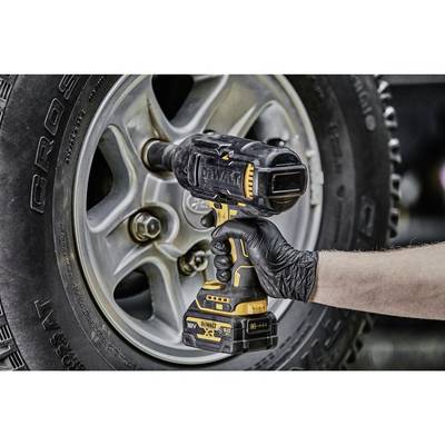 'Rechte Hand mit schwarzem Handschuh hält einen Akkuschlagschrauber und zieht eine Radmutter an der Felge eines Autos an.'