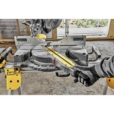Eine Kappsäge mit gelbem Lineal auf Werkbank. Ein Arbeiter in schwarzem Handschuh hält das Werkzeug. Im Hintergrund unscharfe Werkstatt.