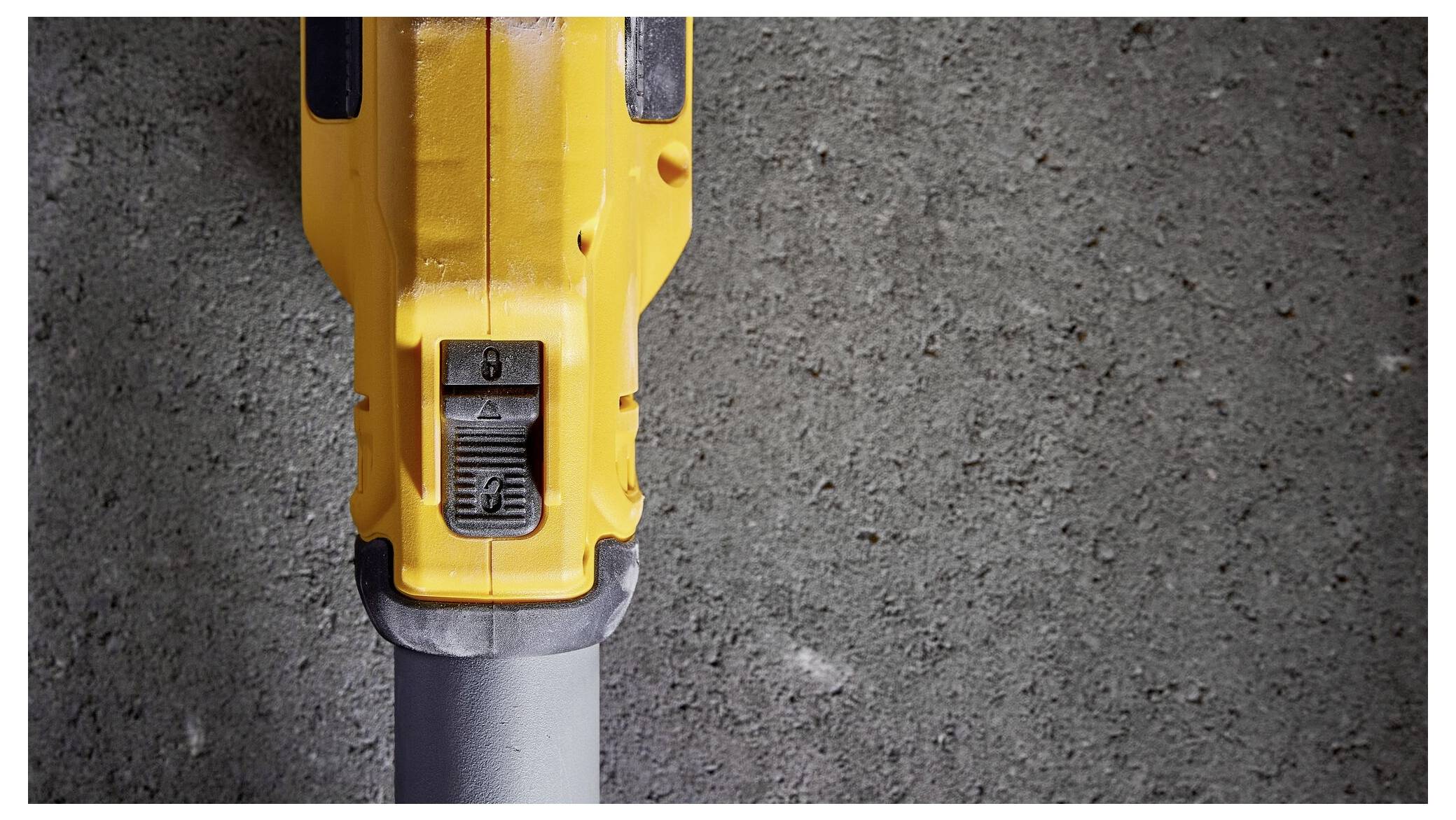 Nahaufnahme eines gelben Elektrowerkzeugs, das auf einer Betonoberfläche steht, Fokus auf den Schalterbereich des Werkzeugs.