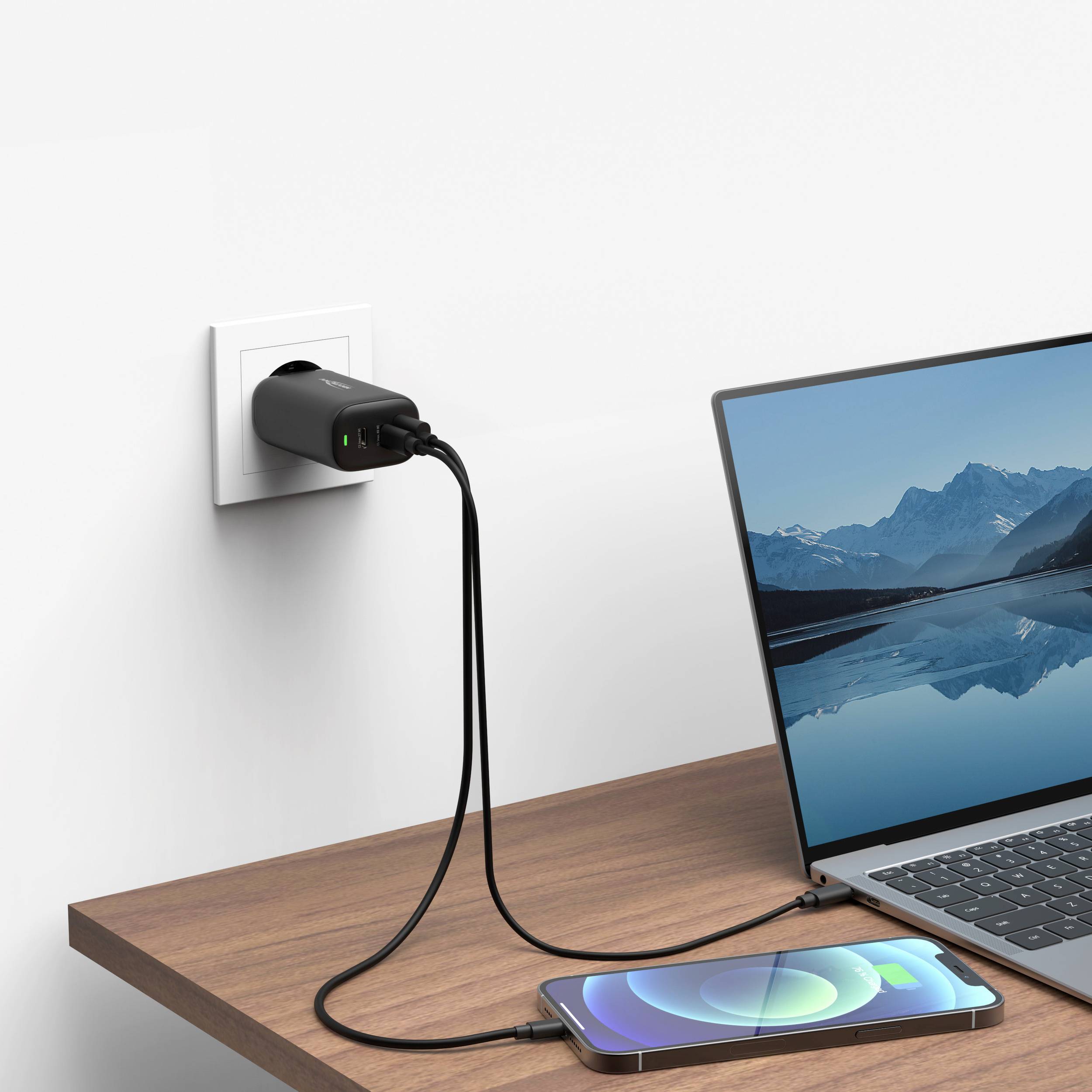 Ein Smartphone auf einem Tisch wird mit einem Kabel an einer Steckdose aufgeladen. Auf dem Handydisplay ist eine Berglandschaft zu sehen.