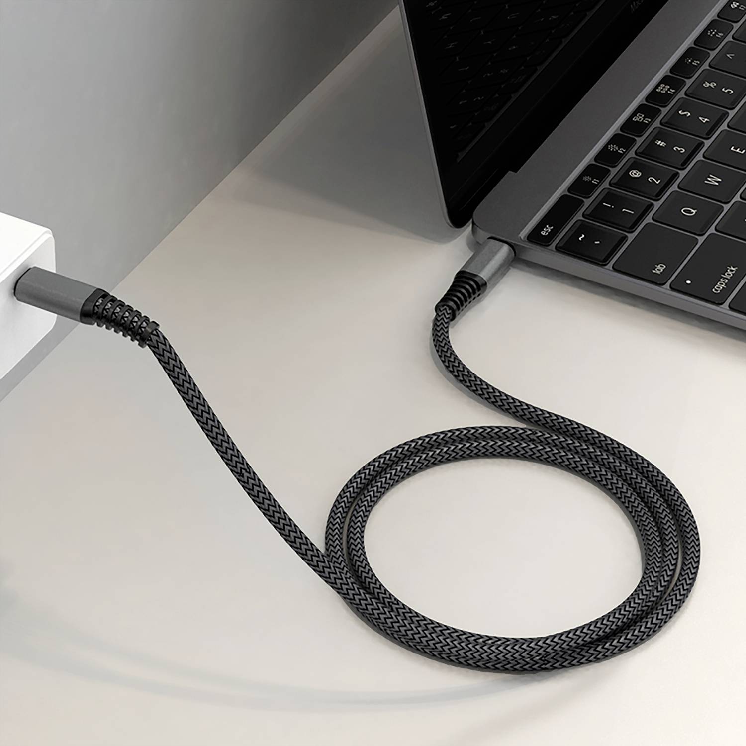 Ein Laptop ist über ein geflochtenes, schwarzes Kabel mit einer Steckdose verbunden. Das Kabel ermöglicht die Stromversorgung des Geräts.
