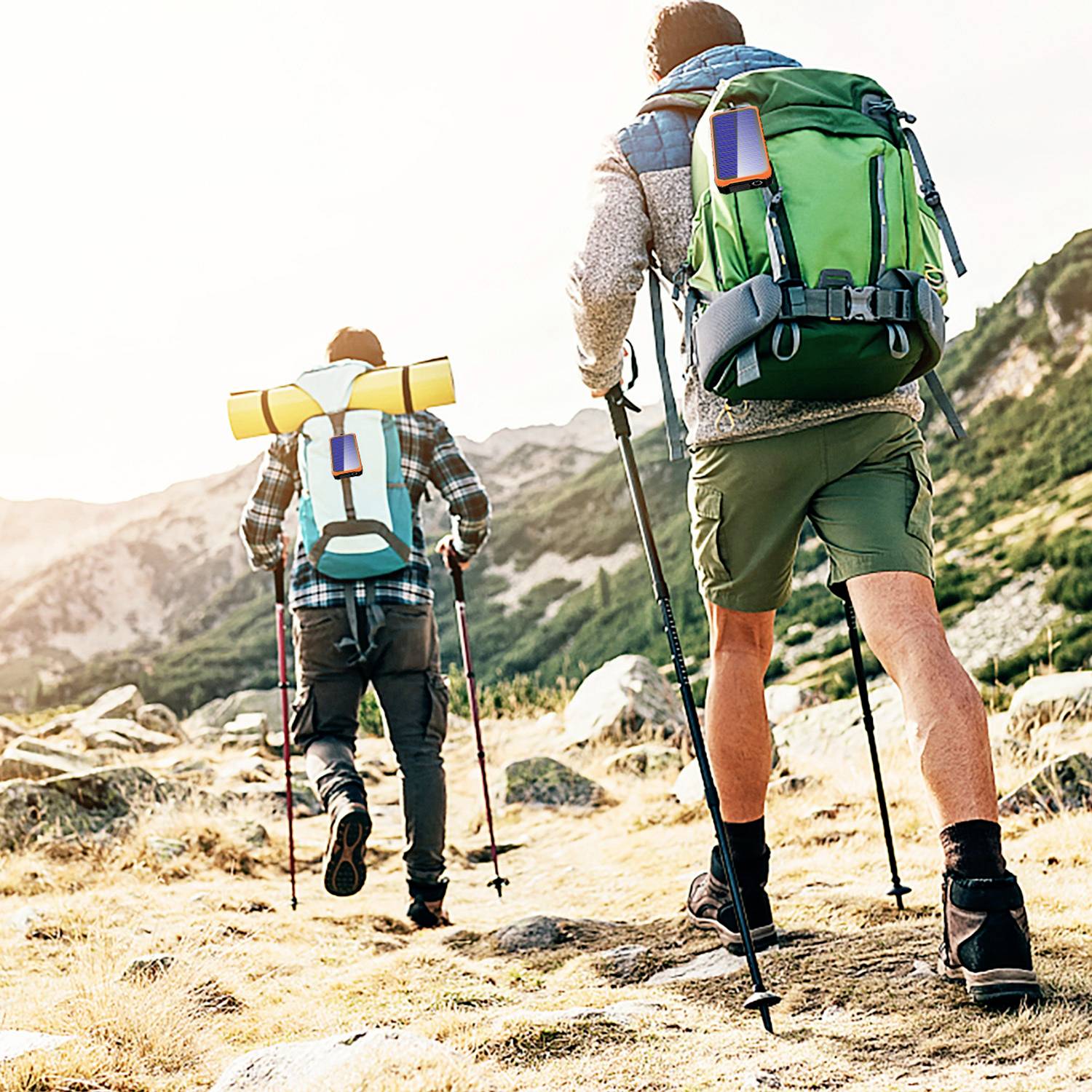 Zwei Personen wandern mit großen Rucksäcken auf einem Bergpfad. Sie sind von einer bergigen Landschaft umgeben und tragen Wanderstöcke.