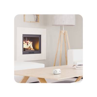 Ein modernes Wohnzimmer mit einem brennenden Kamin, einem weißen Sofa, einem Holztisch und einer Stehlampe. Auf dem Tisch liegt ein kleines weißes Gerät.