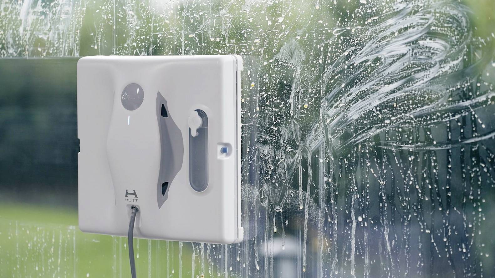 Ein automatischer Fensterputzroboter reinigt ein Glasfenster. Seifenwasser ist sichtbar, während der Roboter über die Oberfläche gleitet.