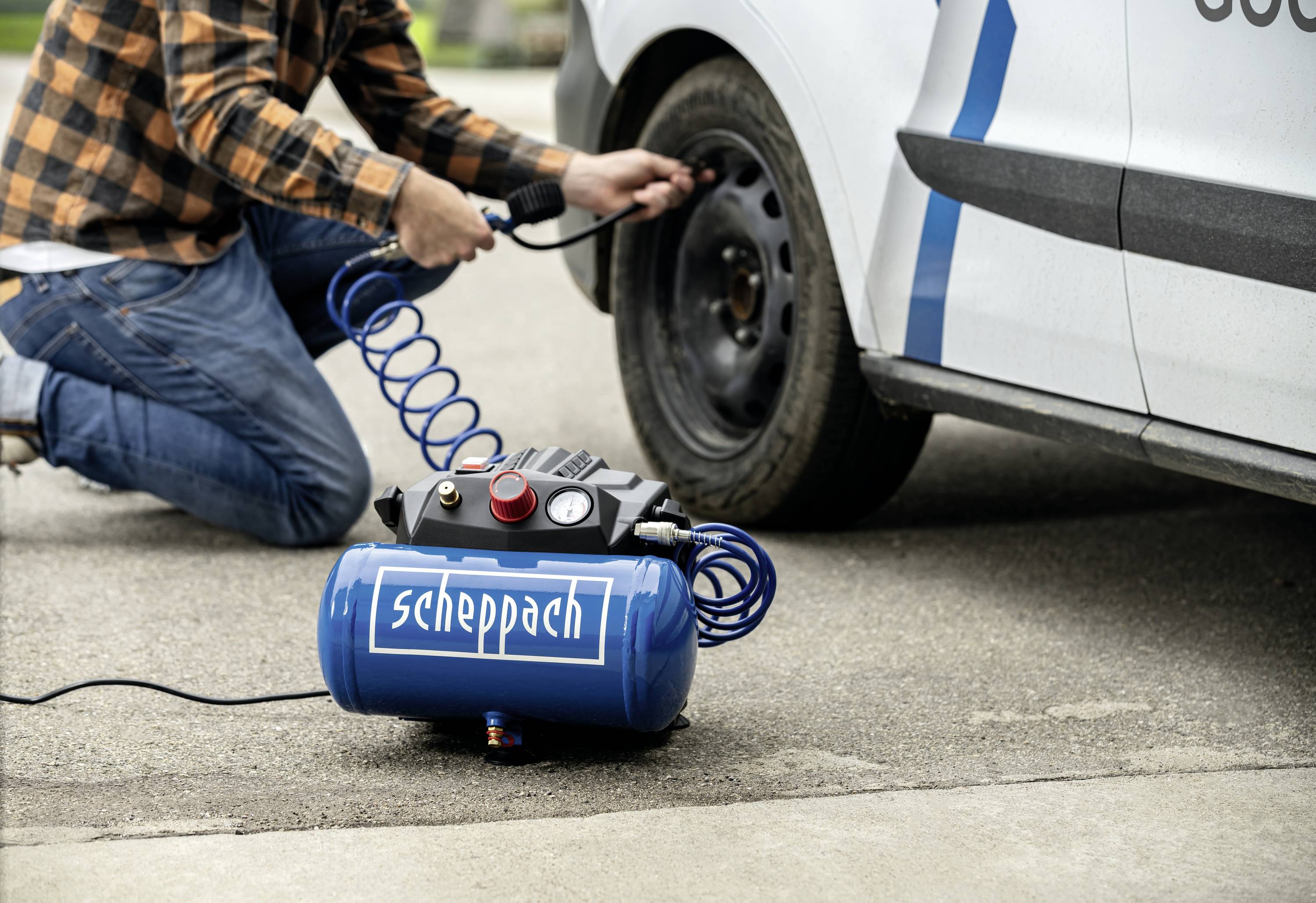 Eine Person pumpt ein Autoreifen mit einem blauen Scheppach-Kompressor auf. Der Kompressor steht am Boden neben dem Auto.