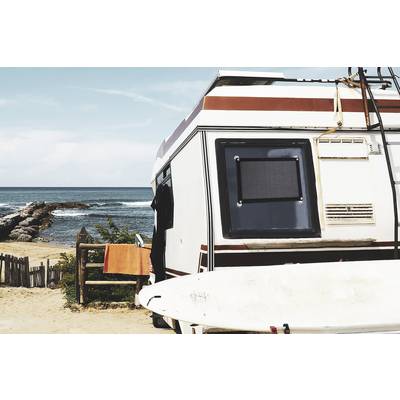 Ein Wohnmobil steht am Strand mit Blick auf das Meer. Ein Surfbrett lehnt an der Seite, ein orangefarbenes Handtuch hängt neben der Tür.
