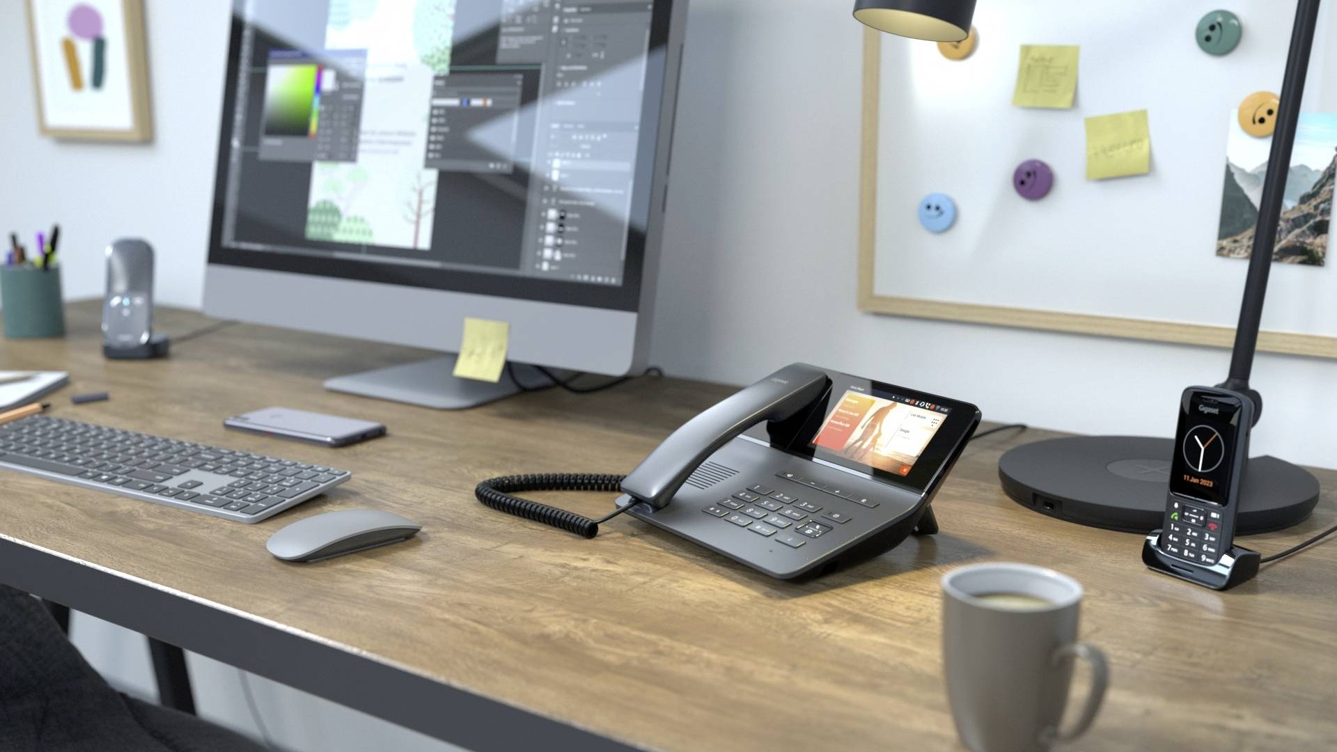 Ein Schreibtisch mit einem Computermonitor, einem schnurlosen Telefon, einer Kaffeetasse und einem modernen Festnetztelefon im Vordergrund.