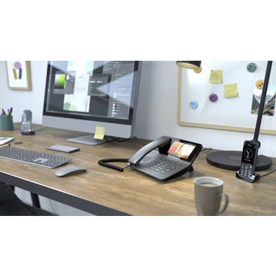 Ein Schreibtisch mit einem Computermonitor, einem schnurlosen Telefon, einer Kaffeetasse und einem modernen Festnetztelefon im Vordergrund.