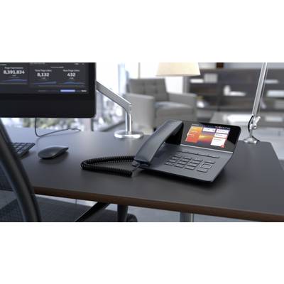 Ein schwarzes Tischtelefon mit großem Display steht auf einem modernen Büro-Schreibtisch neben einem Computerbildschirm.