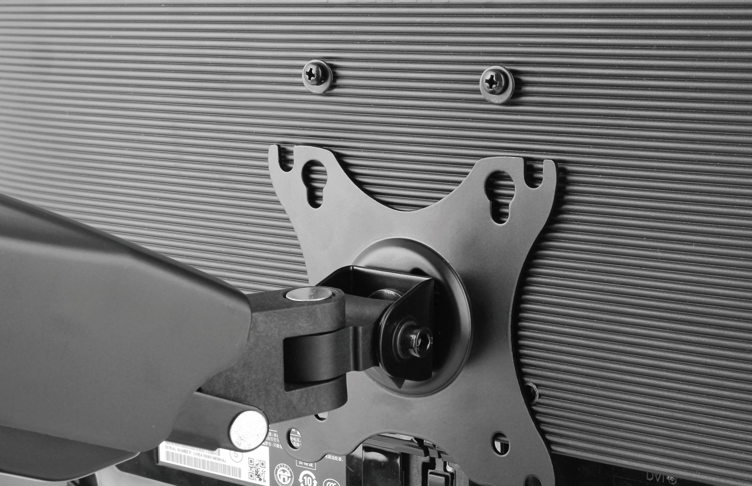 Eine Halterung befestigt einen Flachbildschirm an einem Arm. Die Halterung ist aus Metall und mit Schrauben gesichert.