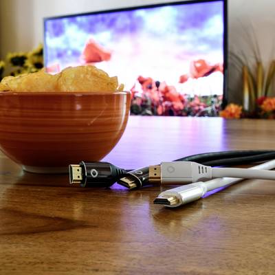 Ein Tisch mit einer Schüssel Chips und verschiedenen Kabeln im Vordergrund. Im Hintergrund läuft ein Film auf einem großen Bildschirm.