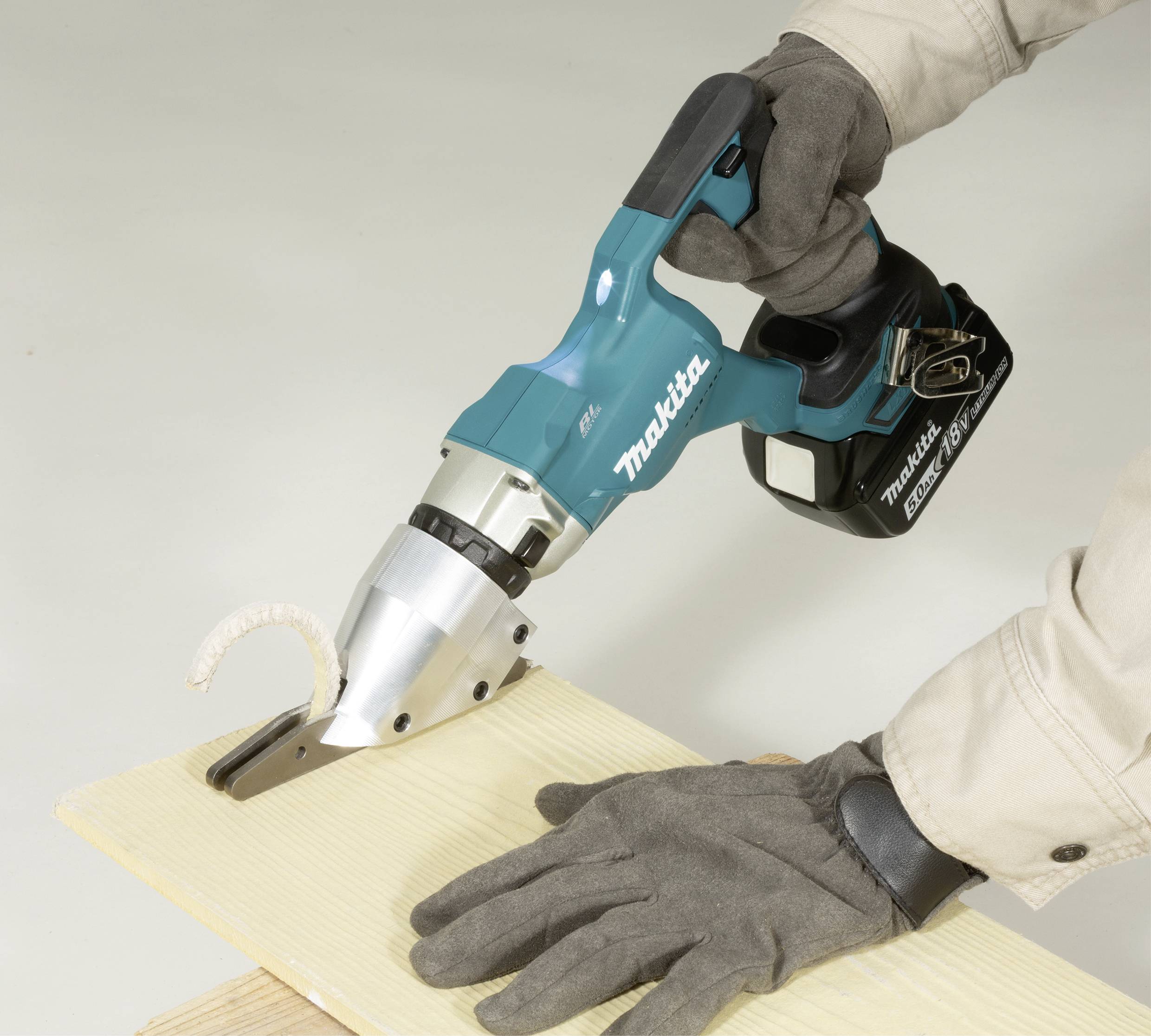 Eine Person schneidet mit einer kabellosen elektrischen Schere ein dünnes Holzbrett. Die Schere erzeugt saubere Schnitte.