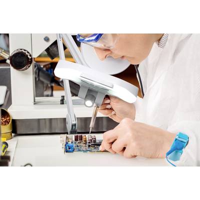 Eine Person in einem Labor arbeitet unter einer Lupe an einer Leiterplatte und verwendet dabei ein Lötkolben, um Bauteile zu befestigen.
