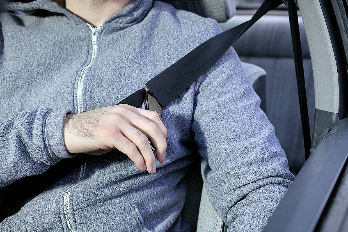 Ein Mann im Auto zieht seinen Sicherheitsgurt an. Der Fokus liegt auf der Handlung, die die Sicherheit betont.