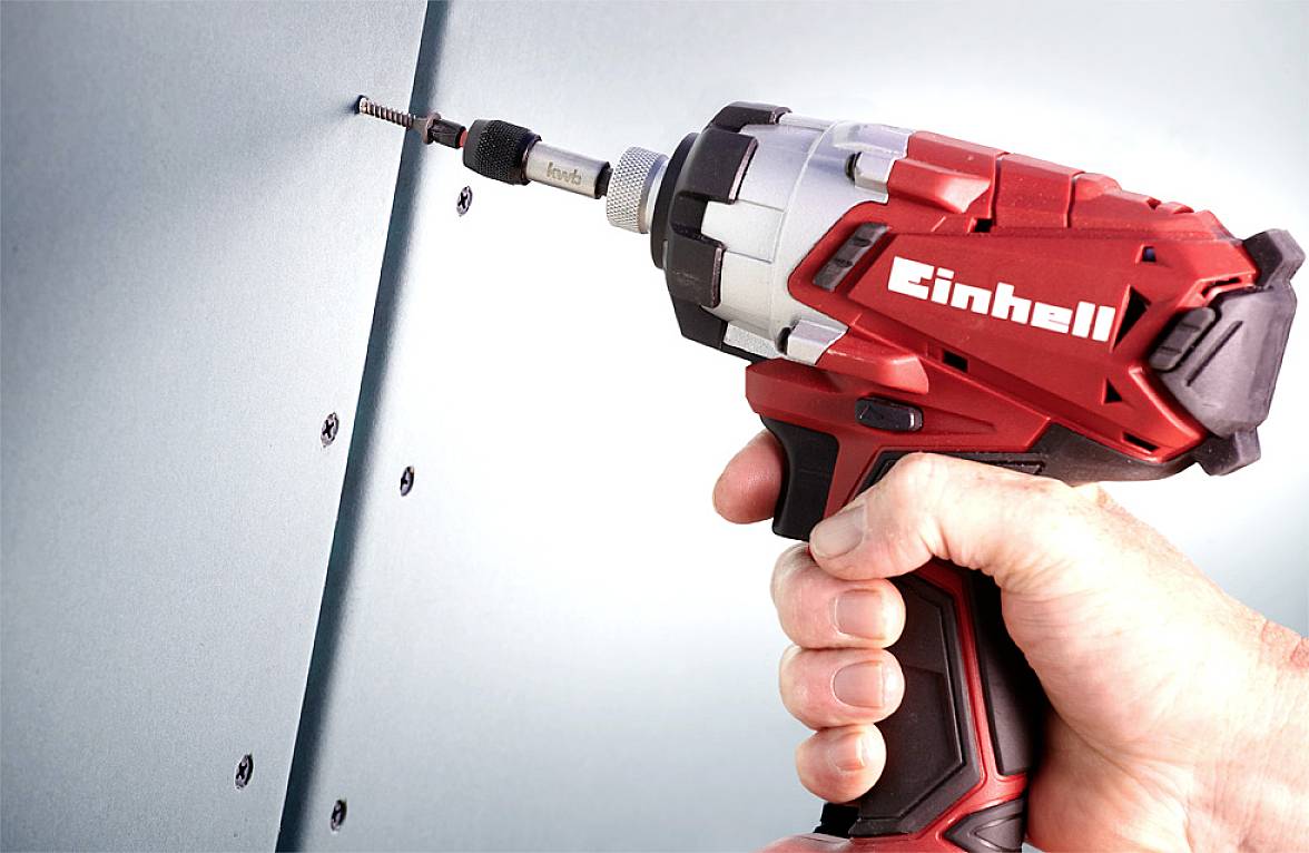 Eine Hand, die einen roten Akkuschrauber hält, schraubt eine Schraube in eine blaue Oberfläche. Der Schrauber ist markiert mit 'Einhell'.