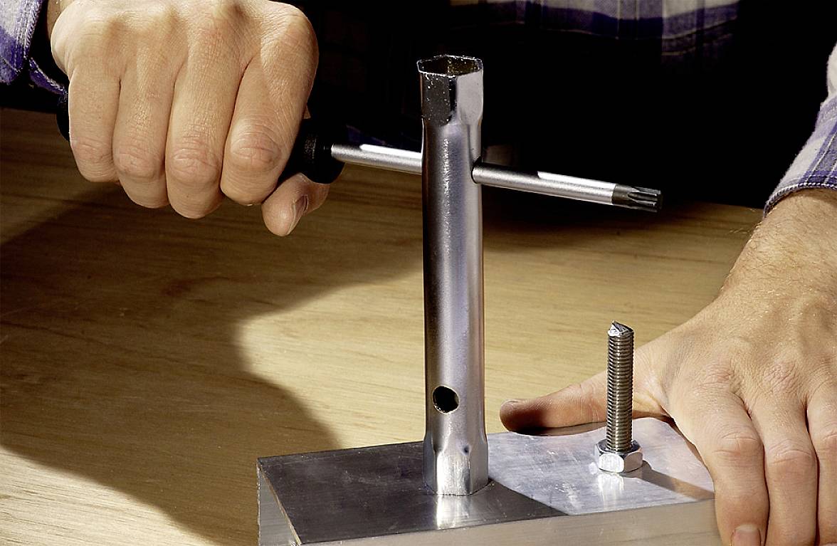 Eine Person benutzt eine Eisenfeile, um das Innengewinde eines Metallrohrs zu bearbeiten, das auf einem Holztisch montiert ist.