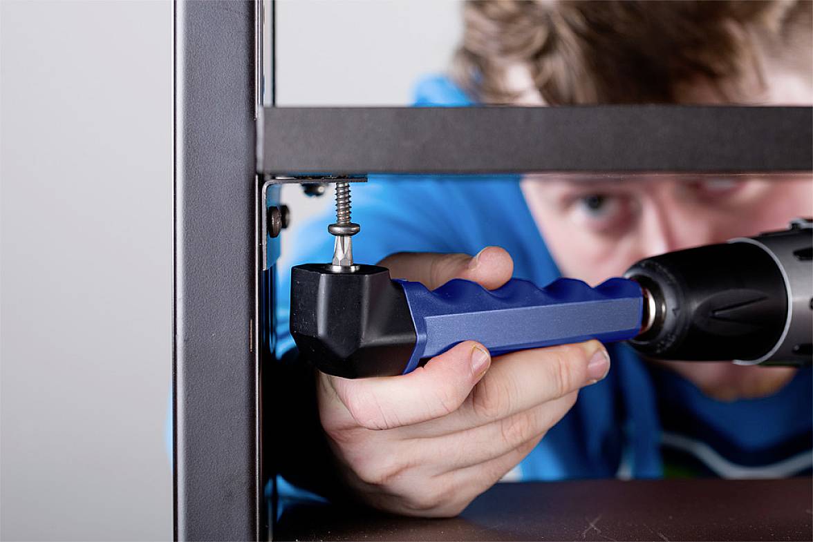 Person befestigt ein Möbelstück mit einem Akkuschrauber und einem blauen Halter. Nahaufnahme zeigt Fokus auf die Schraubarbeit.