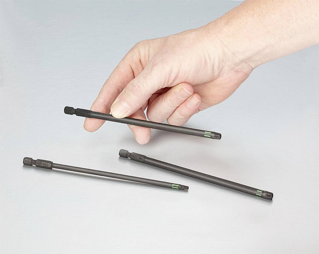 Eine Hand hält eine dünne, schwarze Metallstange, während zwei weitere Stangen auf einem Tisch liegen.