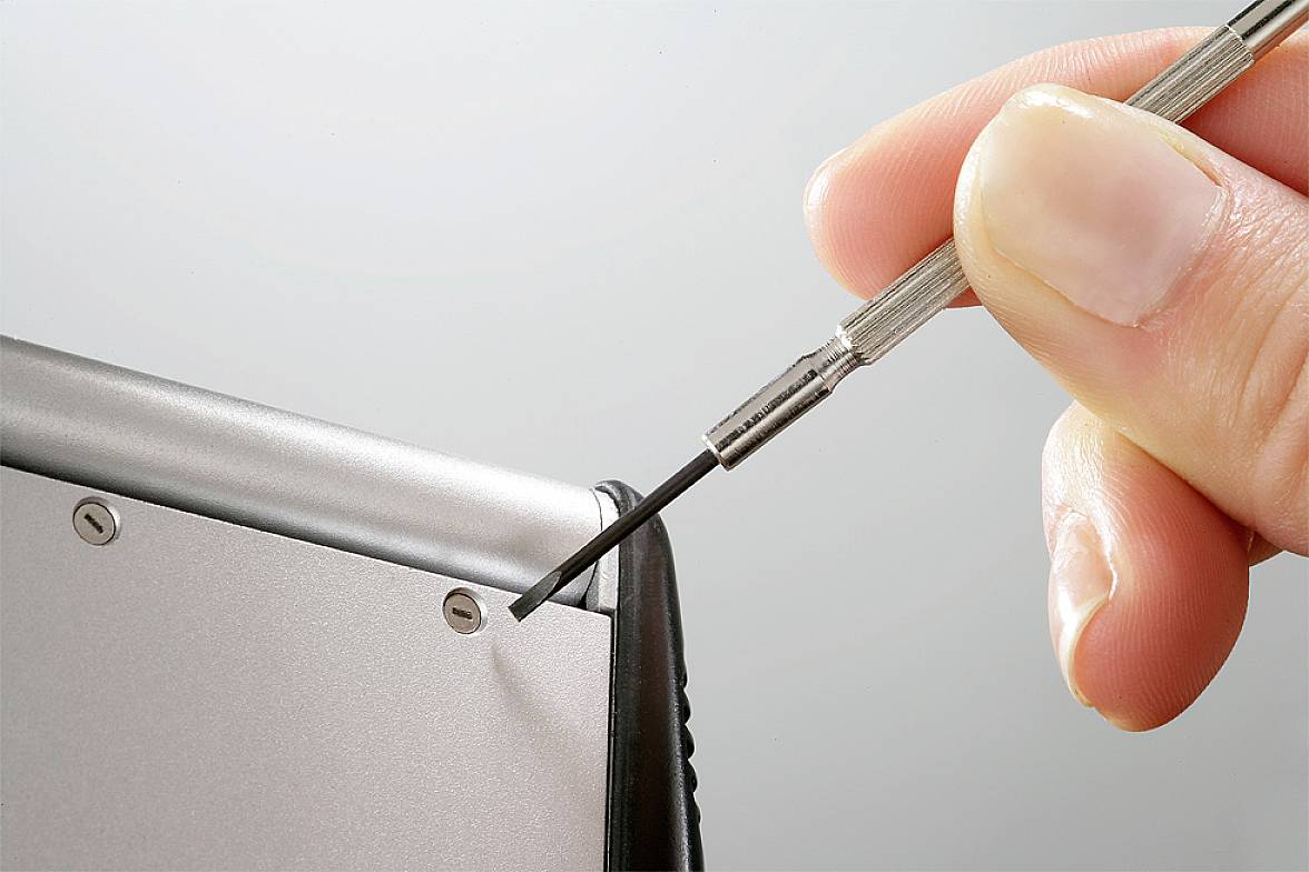 Hand zieht eine Schraube mit einem kleinen Schraubendreher aus einem silbernen Gerät.