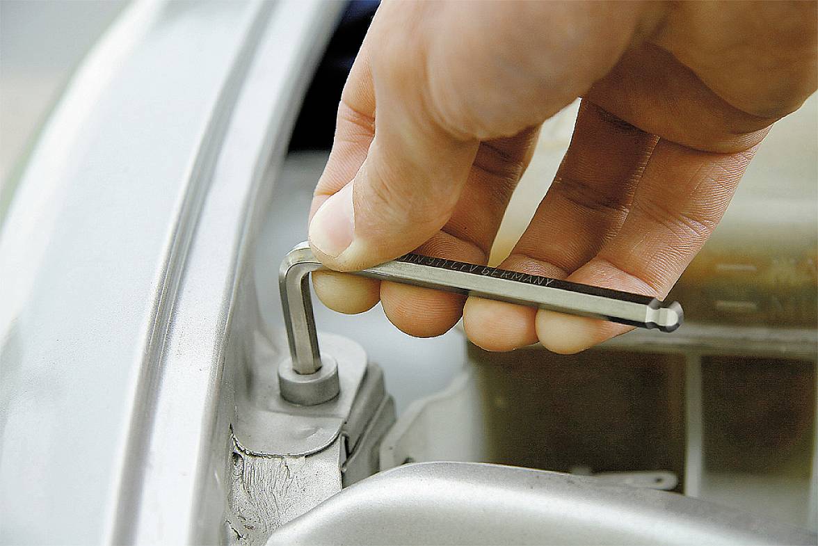 'Nahaufnahme einer Hand, die einen Inbusschlüssel benutzt, um eine Schraube an einem silbernen Metallrahmen festzuziehen.'