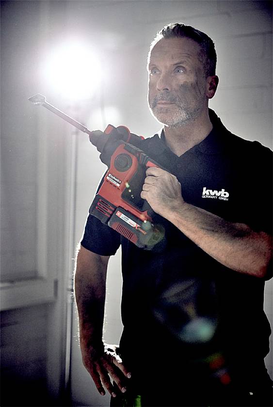 Ein Mann hält einen roten Bohrhammer in der Hand und blickt nach oben. Im Hintergrund ist ein grelles Licht sichtbar.