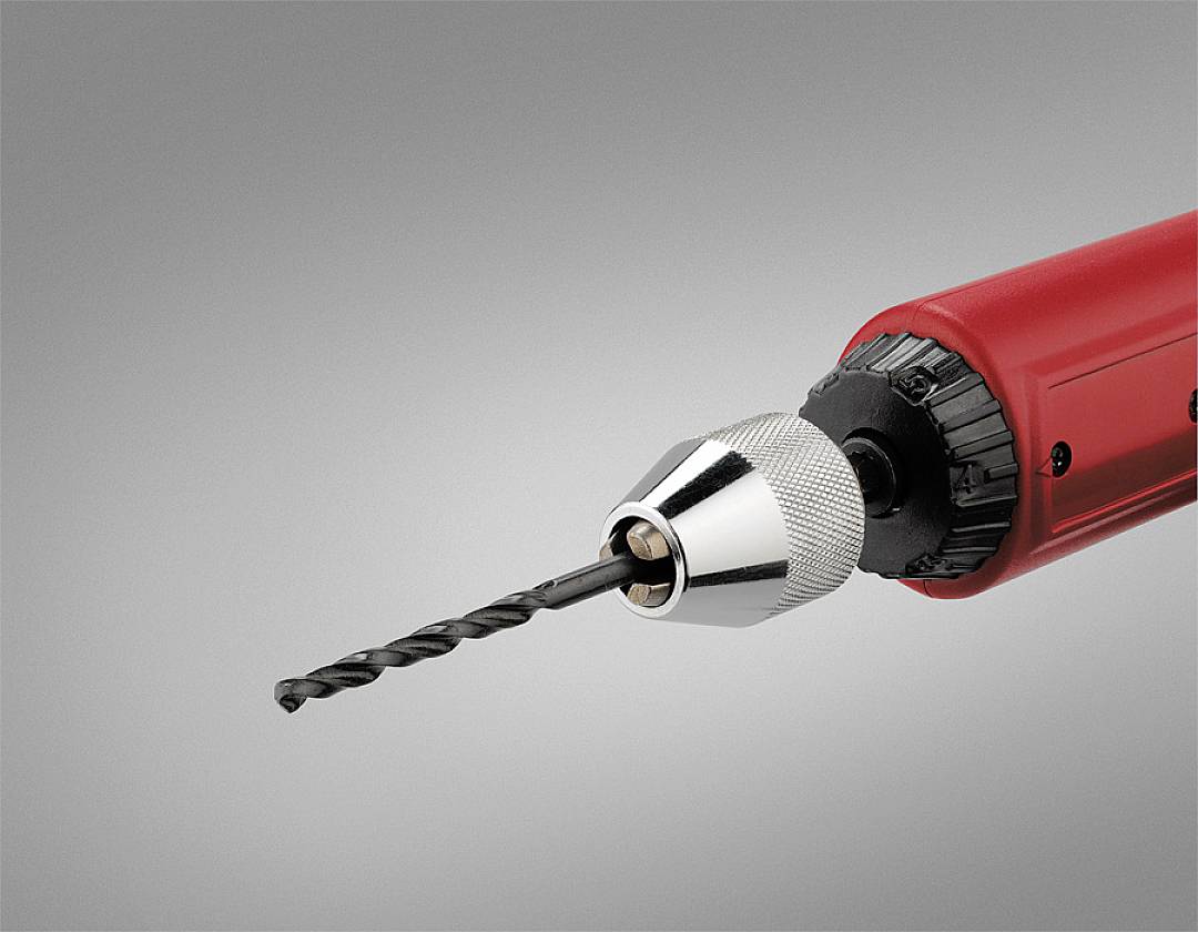 Nahaufnahme eines elektrischen Bohrers mit rotem Gehäuse und eingesetztem Bohrer vor grauem Hintergrund, nach rechts gerichtet.