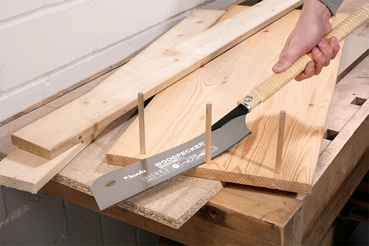 Eine Hand verwendet eine Handsäge mit Holzgriff, um Holzstücke auf einer Werkbank zu sägen.