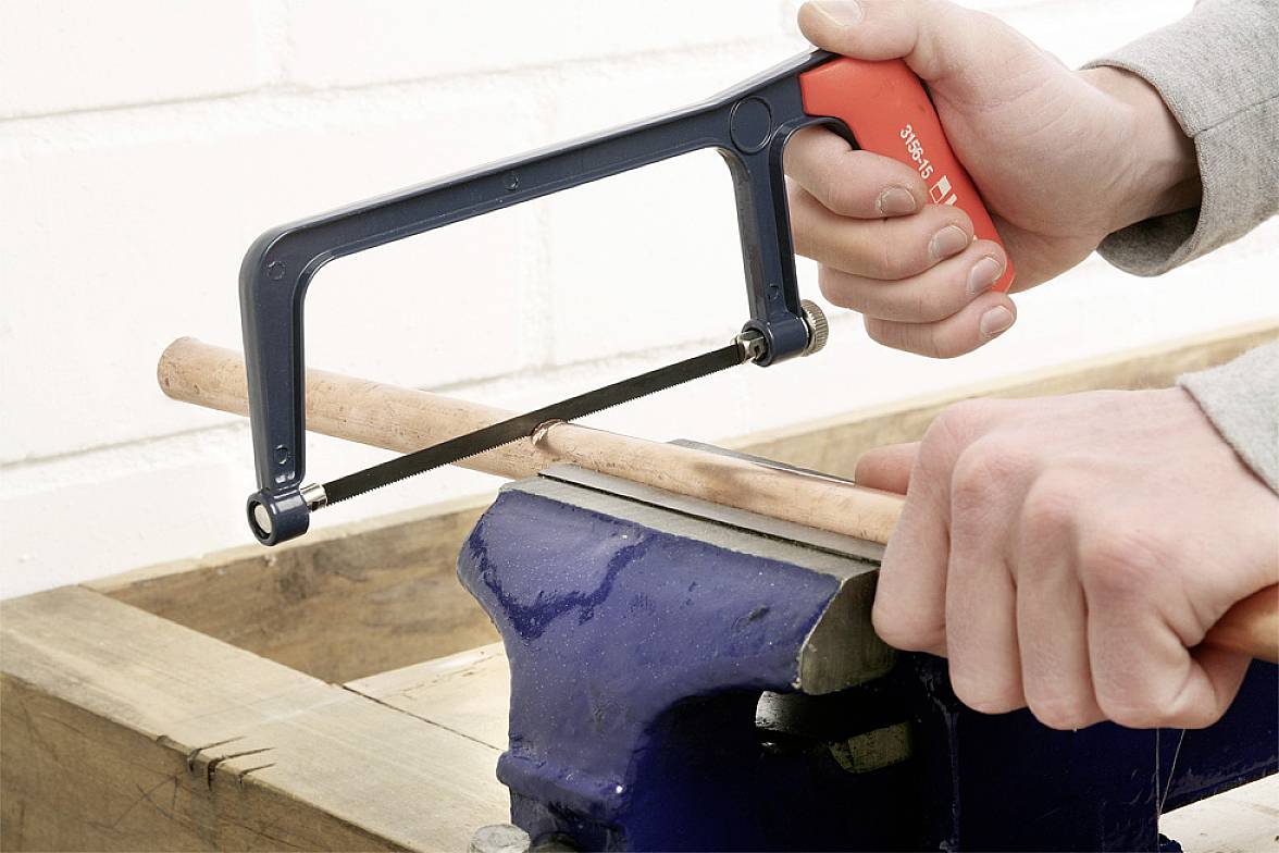 Eine Person sägt mit einer Metallsäge ein Holzstück, das in einem Schraubstock fixiert ist.