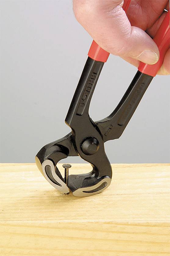 Hand hält einen Seitenschneider, der einen Nagel aus einem Holzbrett zieht.