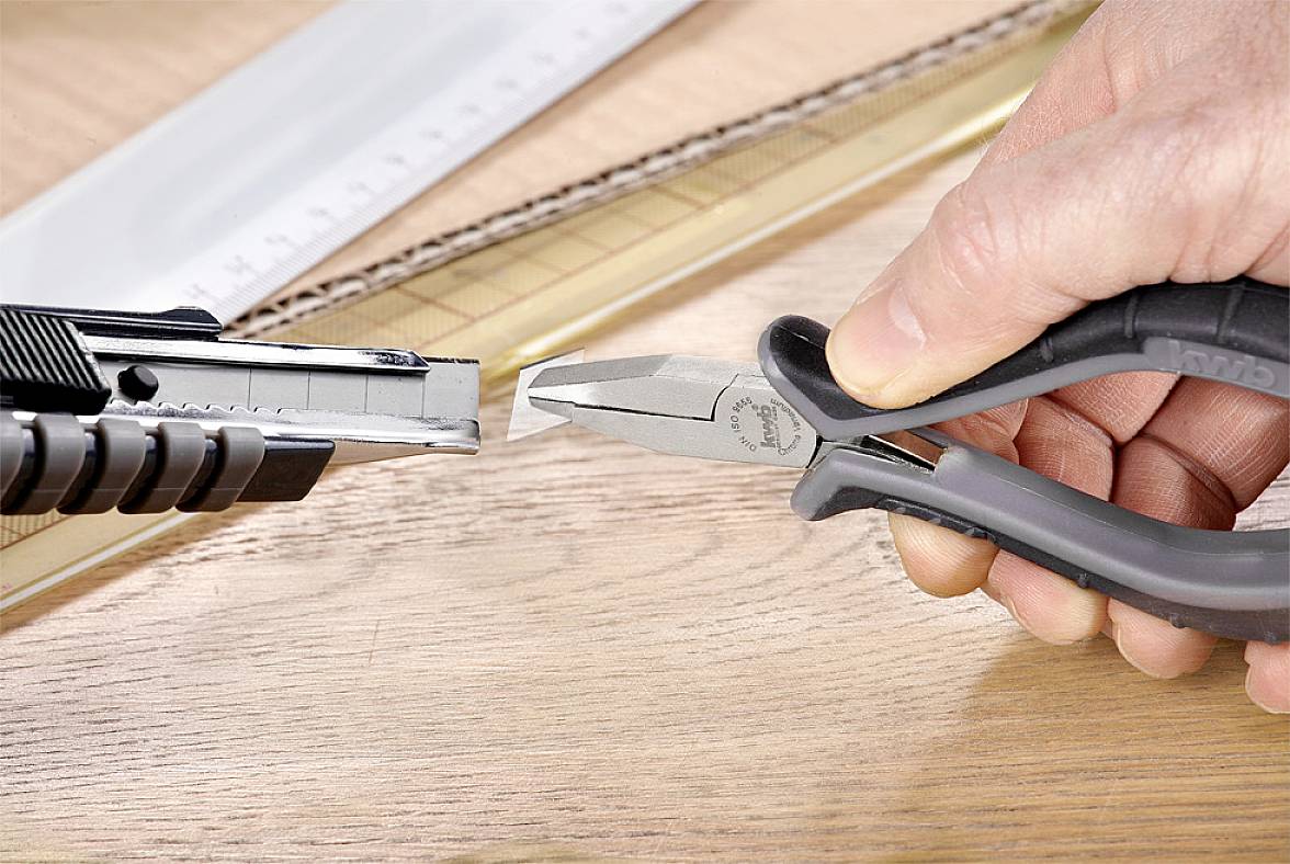 Eine Hand hält eine Zange, die gegen ein Cutter-Messer gedrückt wird. Im Hintergrund sind Lineale sichtbar.