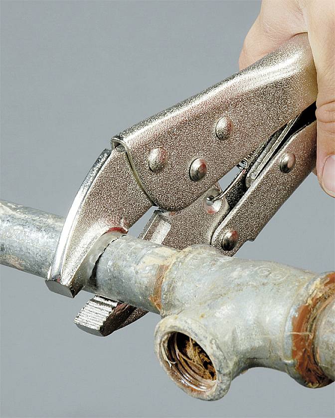 Eine Hand verwendet eine Rohrzange zum Anziehen einer Metallverschraubung auf einem Wasserrohr.