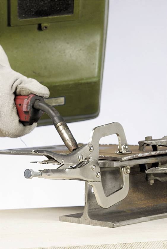 Eine Person schweißt ein Metallstück, indem sie eine Schutzbrille und Handschuhe trägt. Ein Schraubstock hält das Metall sicher fest.