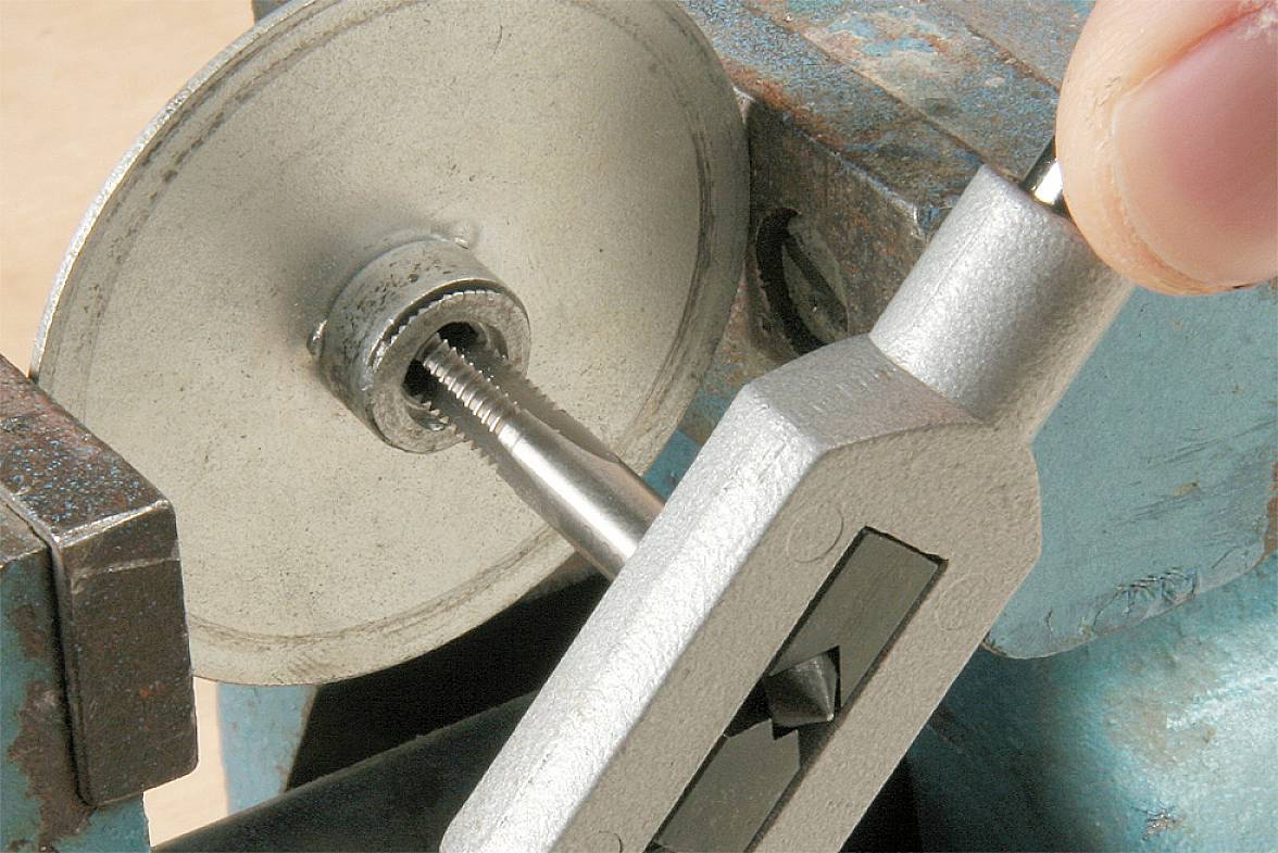 Eine Hand schneidet mit einem Schneideisen ein Gewinde auf einen Metallstab, der in einem Schraubstock eingespannt ist.