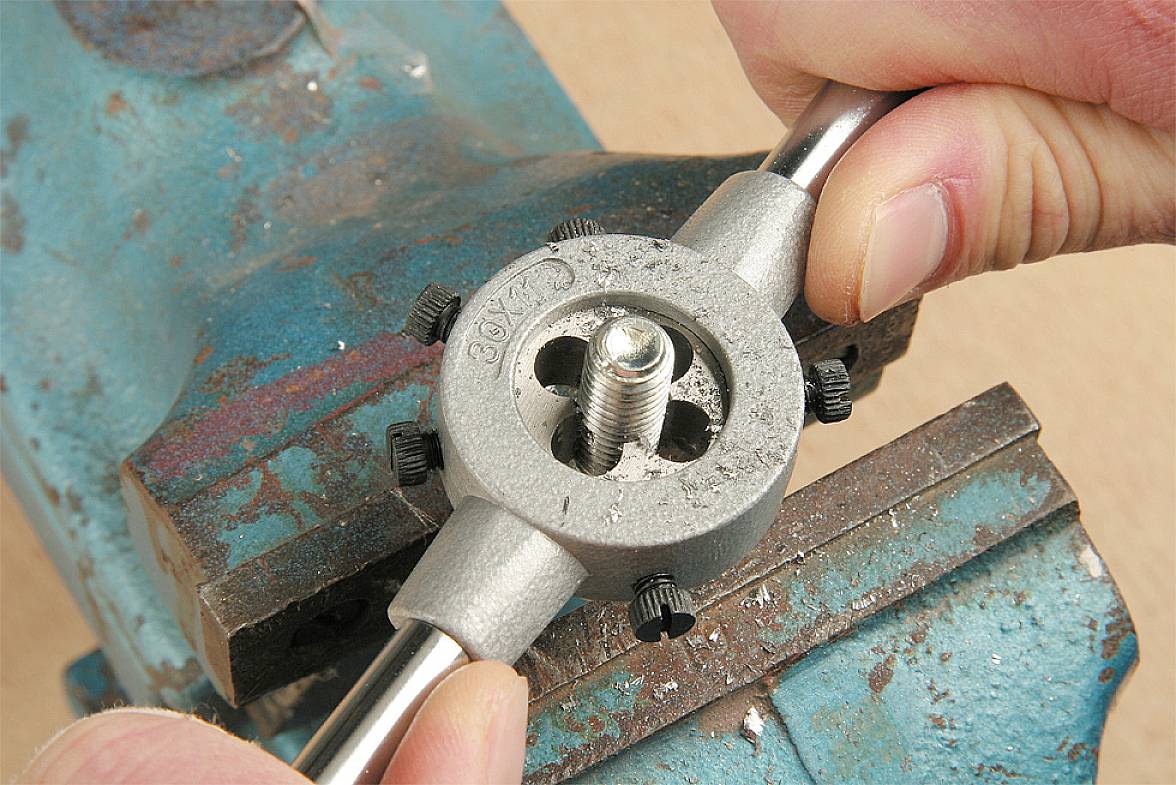 Eine Person schneidet ein Gewinde auf einen Metallstab, indem sie ein Gewindeschneidwerkzeug verwendet, das in einem Schraubstock eingespannt ist.