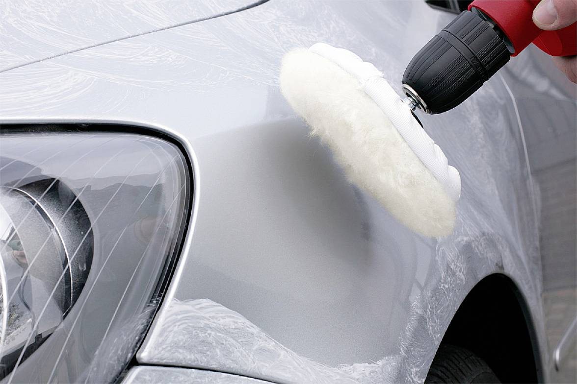 Ein Auto wird mit einer Poliermaschine poliert. Die Maschine ist mit einem weißen Polierpad ausgestattet und wird von einer Hand geführt.