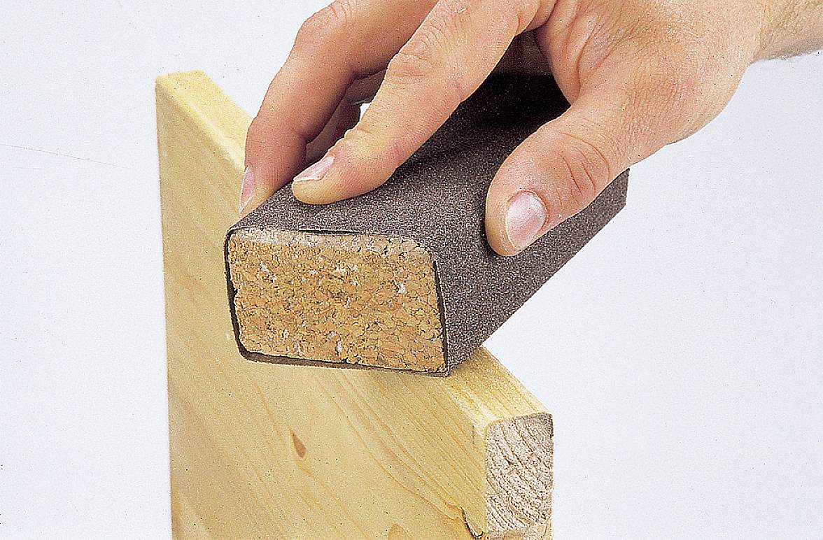 Eine Hand schleift Holz mit einem Schmirgelblock, um die Kanten zu glätten.