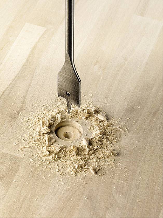 Ein Bohrer erzeugt ein sauberes, rundes Loch in einem Holzbrett. Holzspäne sind um das Loch verstreut.