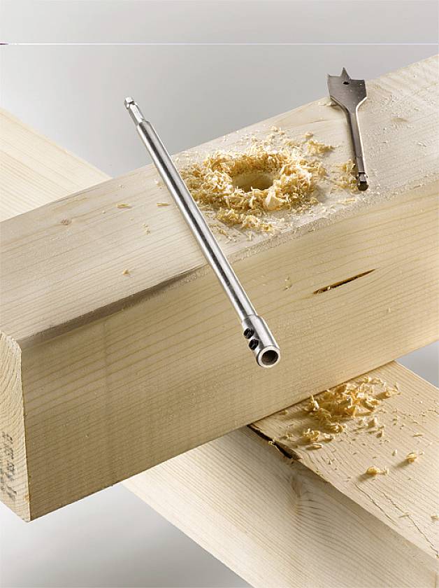 Ein Holzbohrer und eine gebohrte Holzplatte mit Spänen. Ein Flachbohrer liegt daneben.