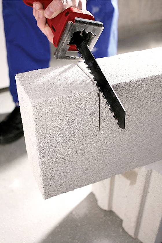 Eine Person schneidet mit einer rot-schwarzen Säge einen Porenbetonblock entlang einer markierten Linie.
