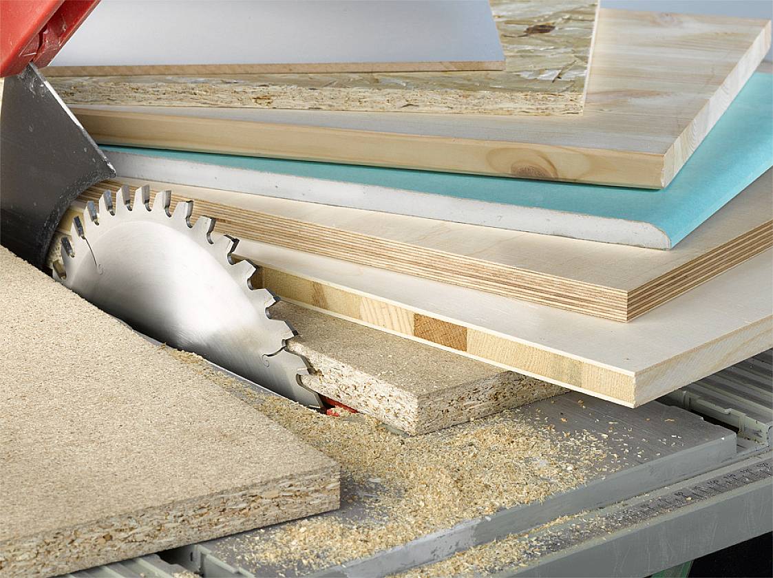 Eine Kreissäge schneidet durch mehrere Holzplatten unterschiedlicher Dicke. Es gibt Holzspäne auf dem Sägeblatt.