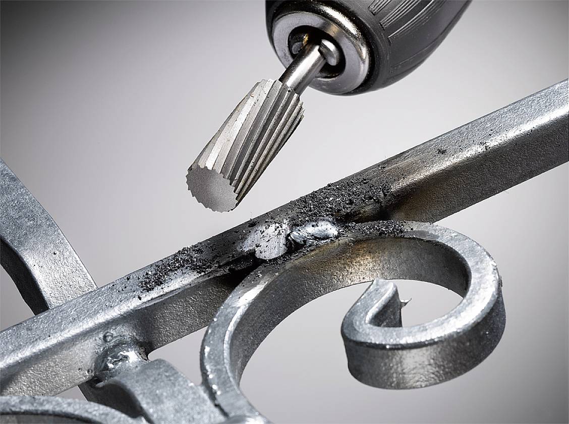 'Ein Dremel-Werkzeug bearbeitet eine metallische Oberfläche, entfernt Rost und glättet die Kanten eines dekorativen Metallgitters.'