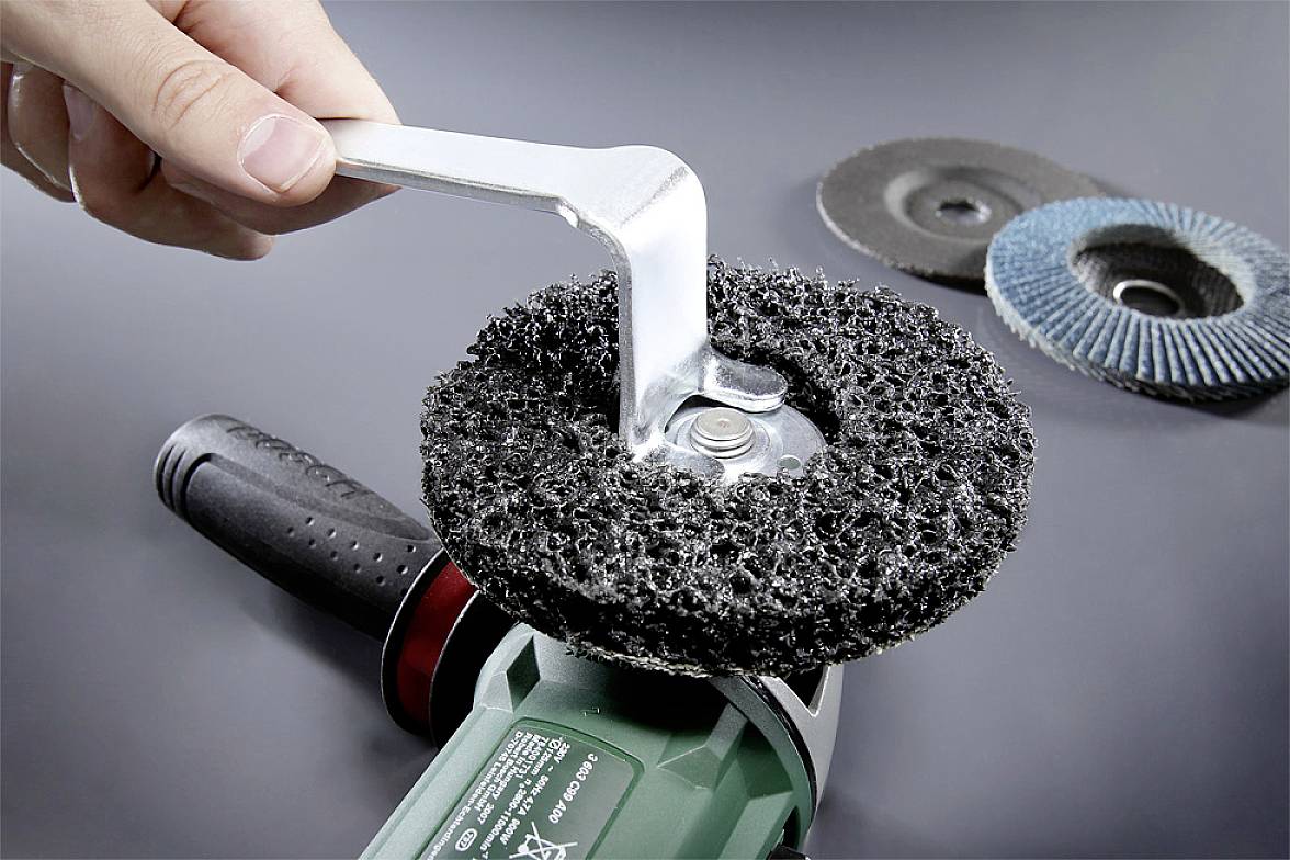 Eine Person befestigt eine Schleifscheibe an einem Winkelschleifer mit einem Schraubenschlüssel, um Schleifarbeiten vorzubereiten.