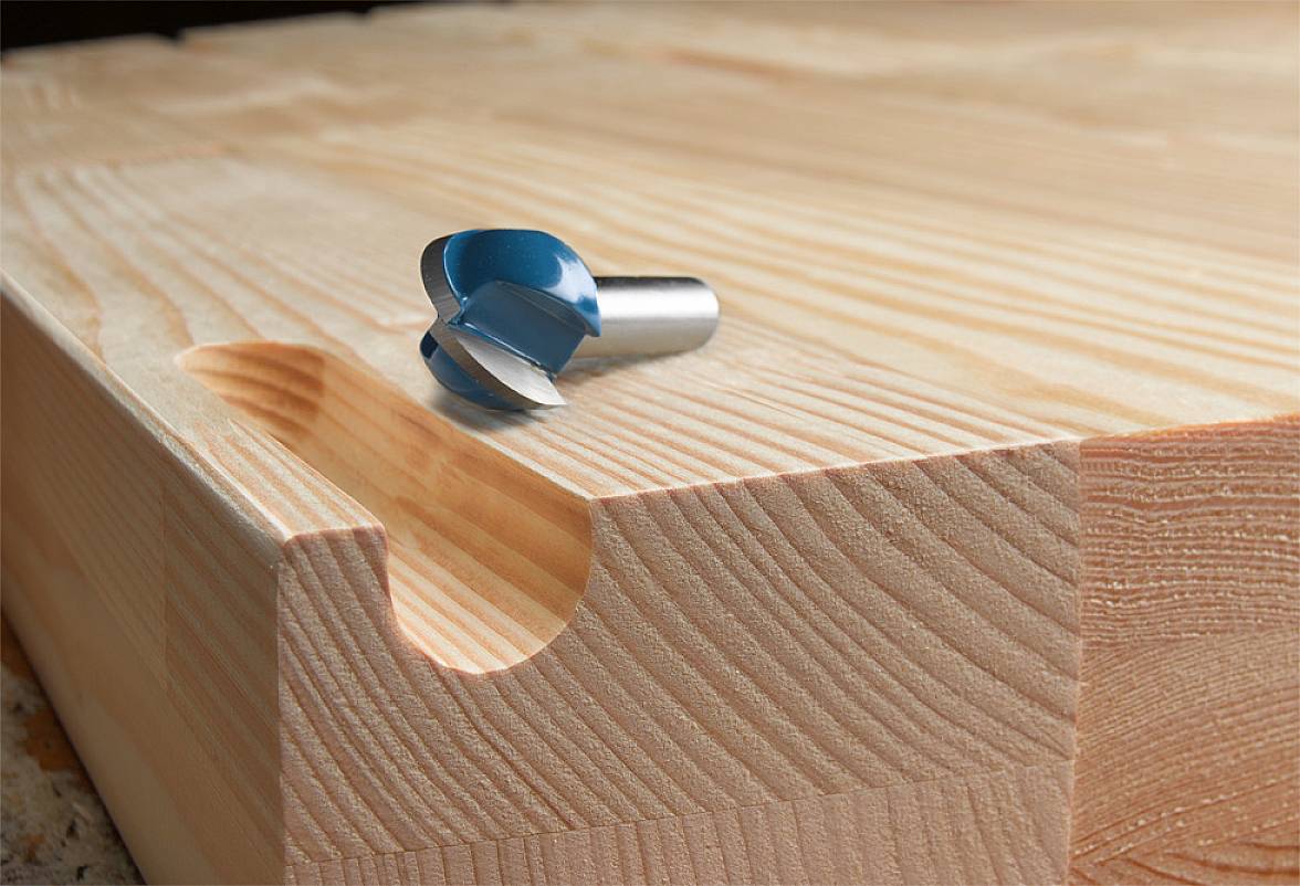 Holzfräsbohrer liegt auf einem Holzbrett mit rundem Ausschnitt. Das Holz hat eine sichtbare Maserung und die Kante ist sauber geschnitten.