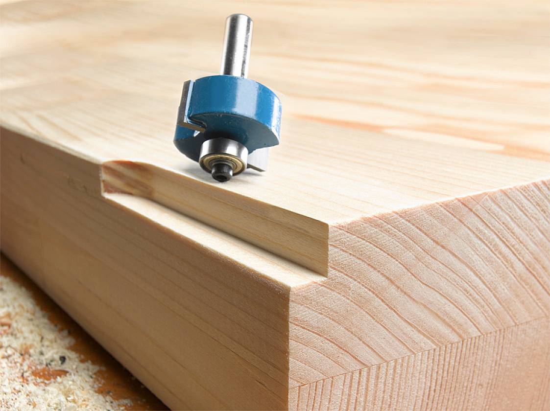 Ein Fräser liegt auf einem Holzblock mit einer gefrästen Nut. Das Bild zeigt ein Beispiel für Holzverarbeitung und Frästechniken.